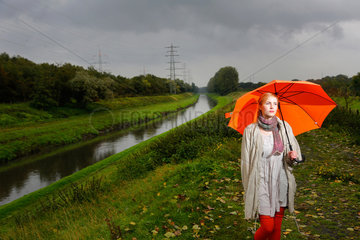 Oberhausen  Deutschland  eine junge Frau geht bei Regenwetter mit Regenschirm an der Emscher spazieren