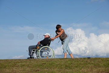 Sankt Maergen  Deutschland  eine Frau schiebt einen Rollstuhl mit aelterem Herrn