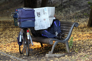 Tokio  Japan  Symbolfoto Armut  ein Mann liegt auf einer Parkbank und liest Zeitung