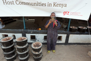 Kakuma  Kenia - Fluechtlingslager Kakuma. Vor einem Banner der GIZ fotografiert ein lokaler Mitarbeiter mit seinem smartphone.