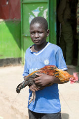 Kakuma  Kenia - Ein Junge mit einem Hahn auf dem Arm.