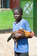 Kakuma  Kenia - Ein Junge mit einem Hahn auf dem Arm.