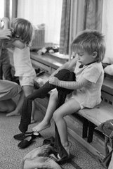 Berlin  DDR  Kind zieht sich in einer Kindertagesstaette seine Strumpfhose an