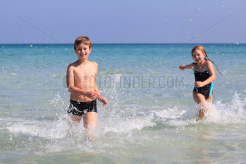 Can Picafort  Spanien  Junge und Maedchen laufen durch das azurblaue Wasser am Strand von Mallorca