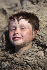 Kaegsdorf  Deutschland  ein Junge steckt bis zum Kopf im Sand