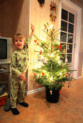 Wendisch Rietz  Deutschland  Junge steht neben einem geschmueckten Weihnachtsbaum