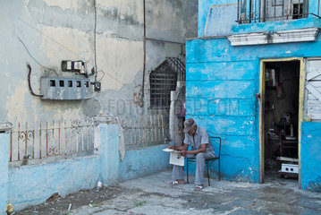 Havanna  Kuba  ein Mann sitzt vor einem Haus und liest Zeitung