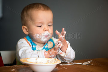 Berlin  Deutschland  ein Kleinkind mit Schnute isst Joghurt mit den Haenden