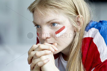 Sports enthusiast watching match with hands clasped in front of mouth