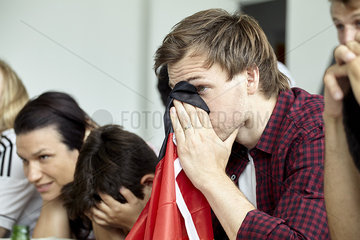 German football supporter covering face with flag while watching match at home