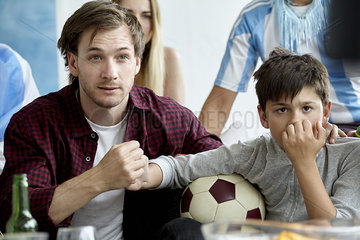 Father and son holding hands while watching football match at home