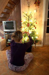 Wendisch Rietz  Deutschland  Frau schmueckt im Sitzen einen Weihnachtsbaum
