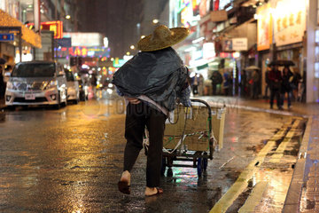 Hong Kong  China  Mann mit Strohhut laeuft bei Regen eine Strasse entlang