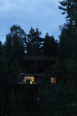 Storsa Lesjoen  Schweden  Holzhaus mit beleuchteten Fenstern am Hang im Wald