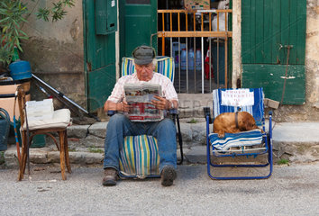 Saignon  Frankreich  ein aelterer Mann sitzt mit seinem Hund am Strassenrand und liest Zeitung