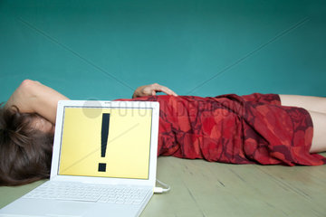 Berlin  Deutschland  eine Frau liegt erschoepft hinter einem Laptop