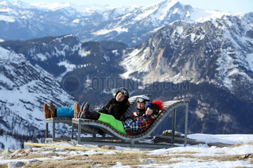 Obertraun  Kinder ruhen sich auf Holzliegen vor dem Panorama der Alpen aus