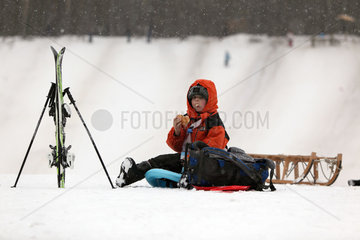 Berlin  Deutschland  Junge macht im Schnee sitzend eine Pause nach dem Wintersport