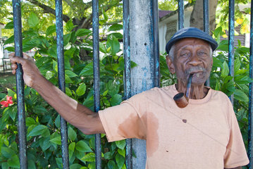Havanna  Kuba  alter Mann mit Pfeife haelt sich an einem Zaun fest