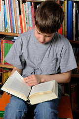 Junge liest Buch vor Buecherregal