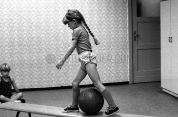 Berlin  DDR  kleines Maedchen steigt im Sportunterricht auf einer Bank ueber einen Medizinball