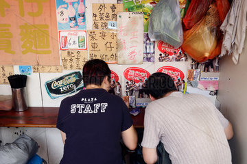 Hongkong  China  zwei Maenner sitzen gebeugt an einem Imbiss und essen