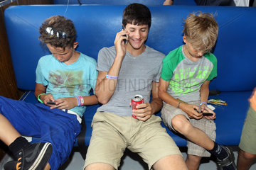 St. Pete Beach  USA  zwei Jungen schauen auf ihre Smartphones waehrend ein Dritter telefoniert