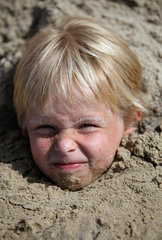 Kaegsdorf  Deutschland  ein Junge steckt bis zum Kopf im Sand