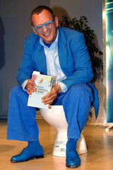 Schriftsteller Peter Roos praesentiert sein Buch Du pinkelst ja im Sitzen auf der Mainfranken-Messe in Wuerzburg auf einer Kloschuessel sitzend