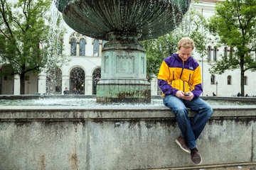 Muenchen  Deutschland  Student sitzt am Brunnen am Geschwister-Scholl-Platz