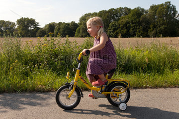 Ruehstaedt  Deutschland  ein Maedchen auf einem Fahrrad mit Stuetzraedern