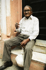 Havanna  Kuba  Mann mit Zigarre sitzt laechelnd auf den Stufen eines Hauseingangs