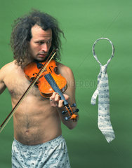 Berlin  Deutschland  Mann mit nacktem Oberkoerper laesst mit siener Geigenmusik eine Krawatte schweben