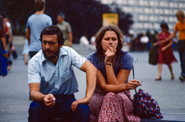 Berlin  DDR  Frau und Mann sitzen rauchend auf einer Strassenbank