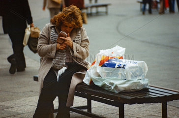 Berlin  DDR  Frau sitzt auf einer Strassenbank und zuendet sich eine Zigarette an