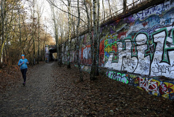 Berlin  Deutschland  Frau joggt an einer mit Graffiti bespruehten Mauer entlang