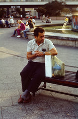 Berlin  DDR  Mann sitzt mit seinen Einkaeufen auf dem Alexanderplatz auf einer Bank