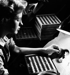 A female employee in profile tests a glass valve bases at Mullard Ltd  1963.