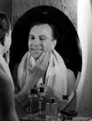 Man looking into a mirror admiring his face after shaving  c 1950s.