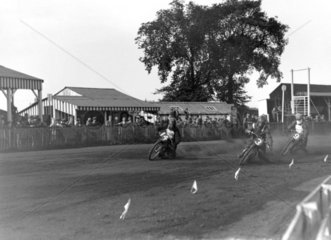 Speedway riders rounding a dirt-track corne