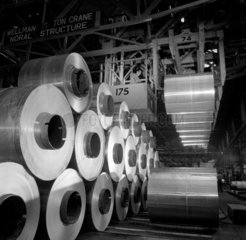 Rows of parked aluminium coils and lifting beam with operator in crane  1961.