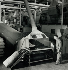 Employee on long conveyor belt loads bags of raw asbestos material  1961.