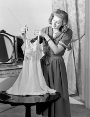 Woman in bedroom holding up a nightie  c 1930s.
