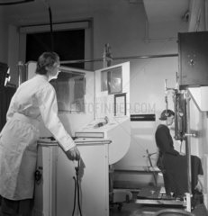 Female radiographer operates X-ray machine from behind screen  1952.