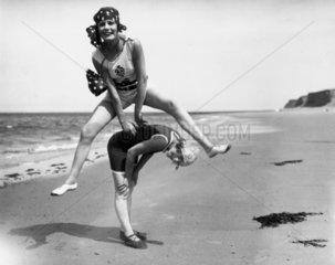 Two women in bathing costumes playing leapfrog on the beach  c 1920s.