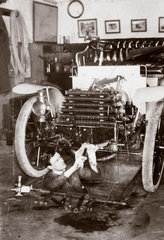 C S Rolls standing in a garage pit working on the engine of a car  c 1900.