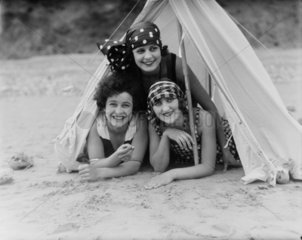 Three women wearing the latest summer fashions lying prone in a tent  c 1920s.