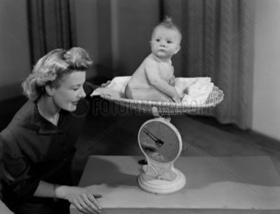 Woman weighing a baby on a pair of scales  c 1949.