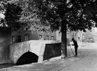Man painting beneath a tree by a bridge c.1930s