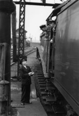 Driver and fireman consulting with station guard  c 1956.